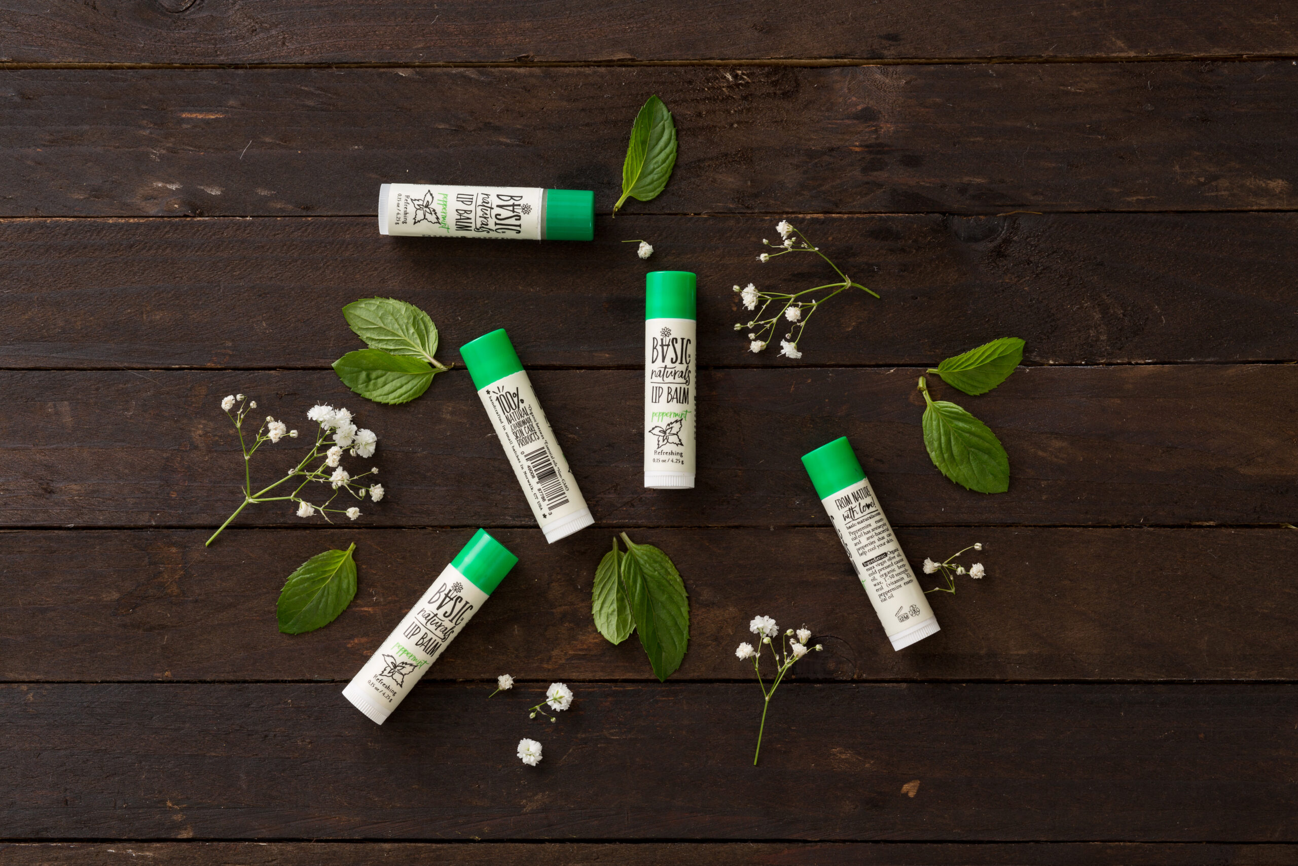 Ultimate Lip Treatment - Peppermint Scented Lip Balm Artistic Photograph of 5 Products with Peppermint Leaves and Natural dark wood background