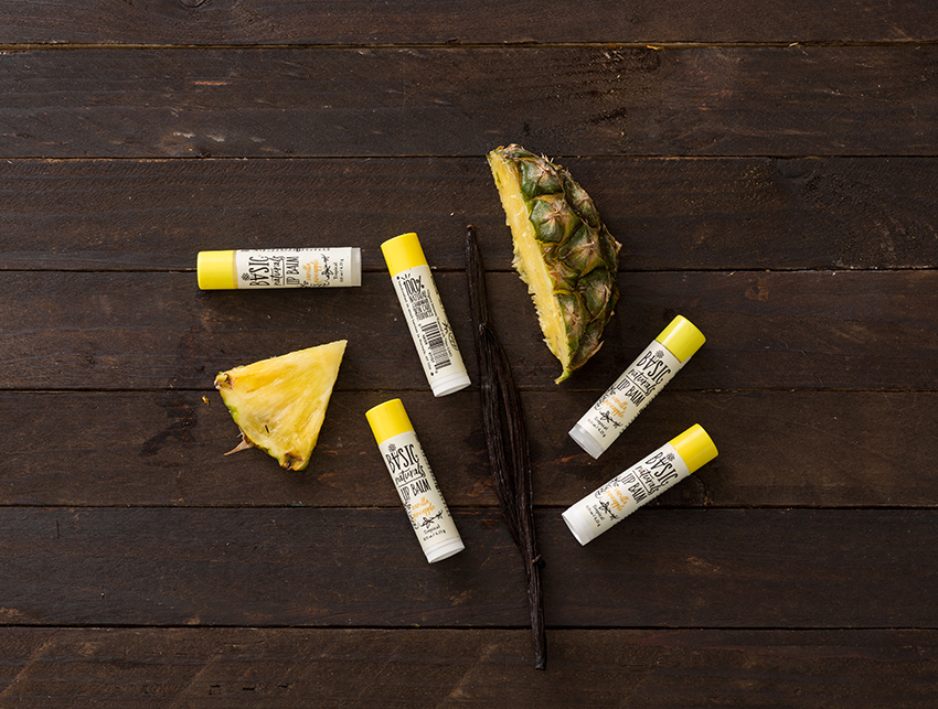 Ultimate Lip Treatment - Vanilla Pineapple Scented Lip Balm Artistic Photograph of 5 Products with Fruit Pieces on dark wood background